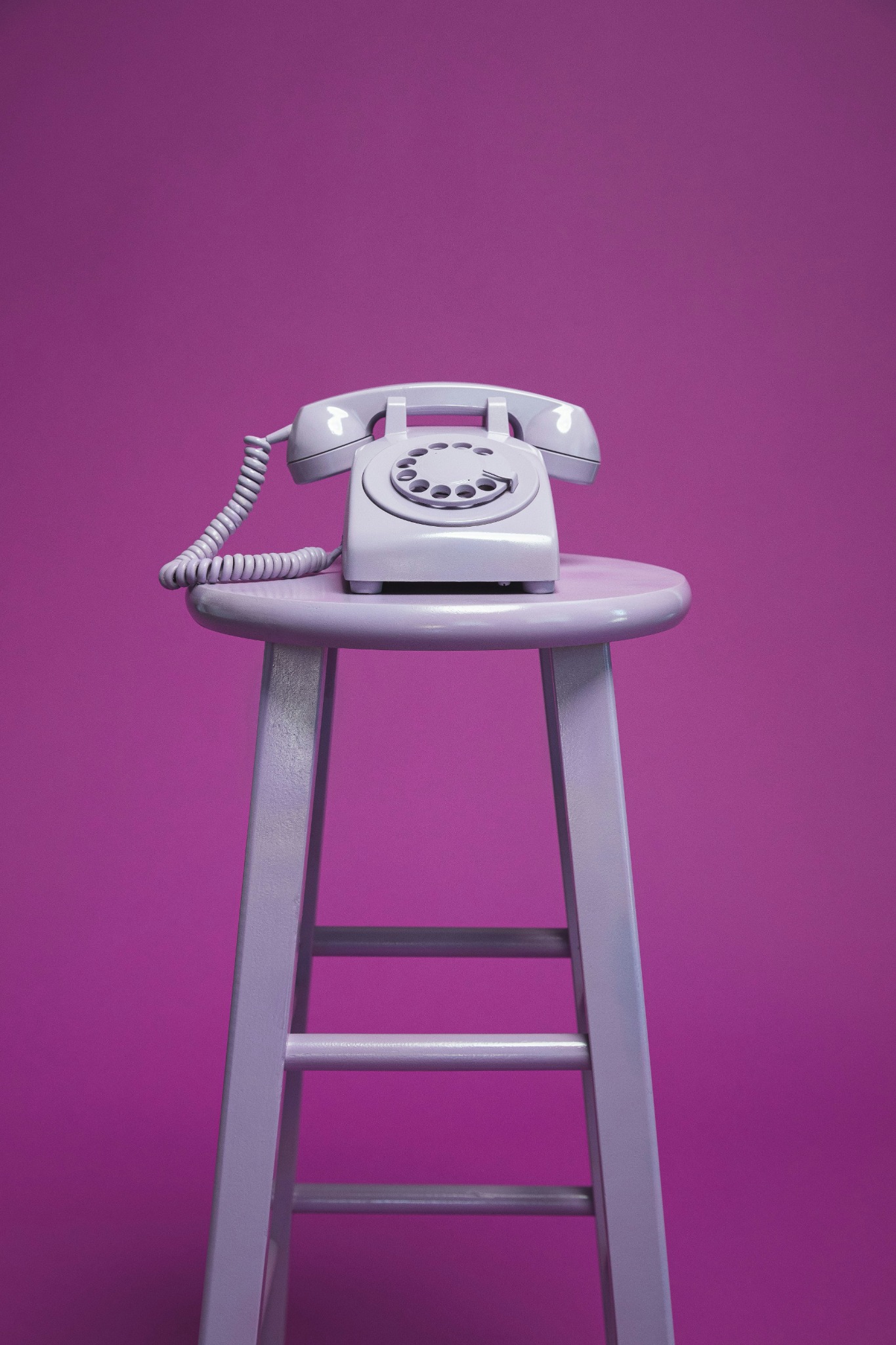 A lavender rotary telephone on a stool against a vibrant purple background