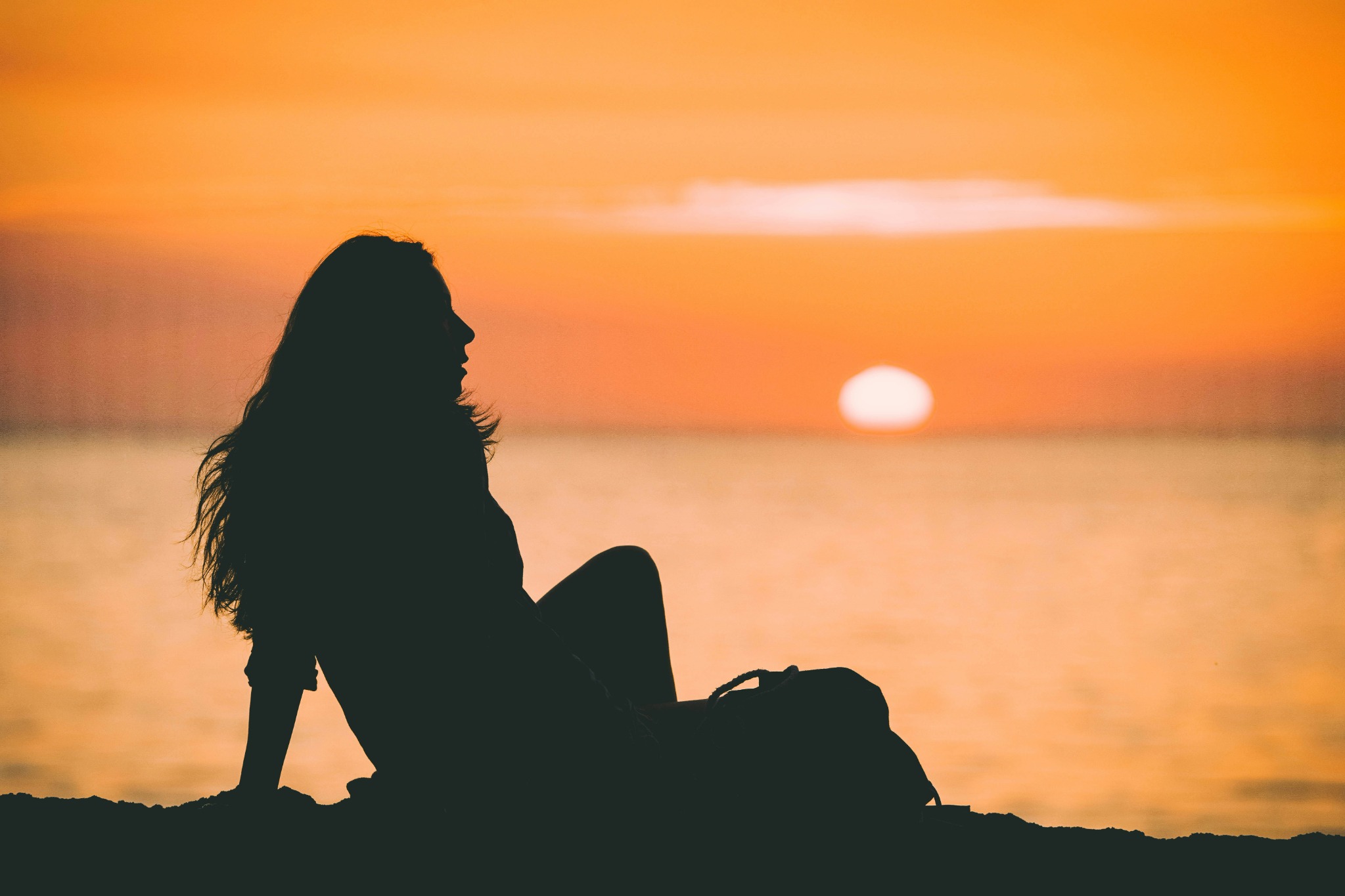 A woman’s silhouette beside the water at a golden sunset